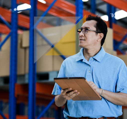 Hombre con gafas en un almacén industrial sosteniendo una carpeta, con estanterías llenas de cajas y productos.