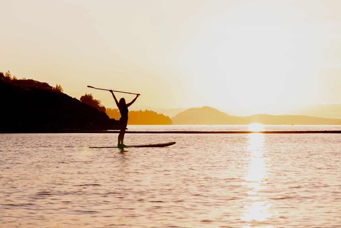 Person paddleboarding during sunset on a lake with hills in the background.