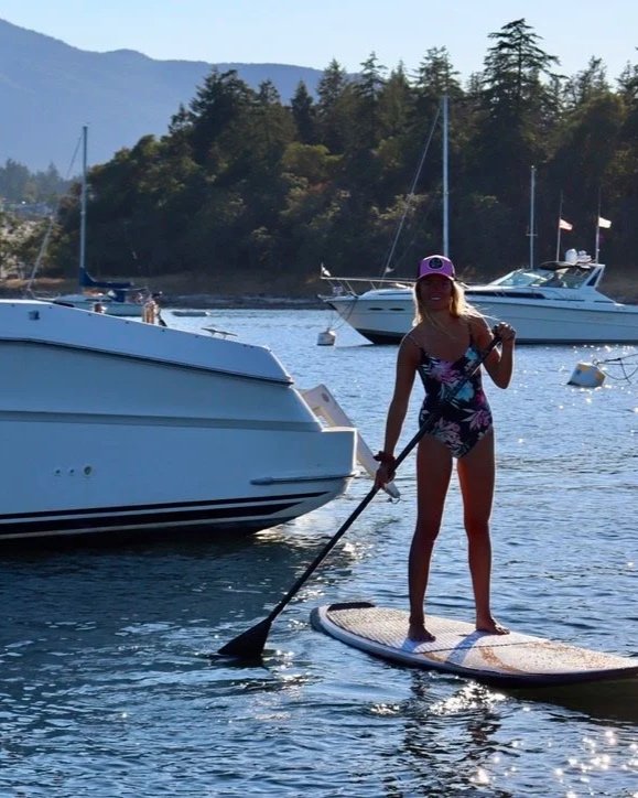 Woman paddleboarding on a lake with boats and trees in the background.