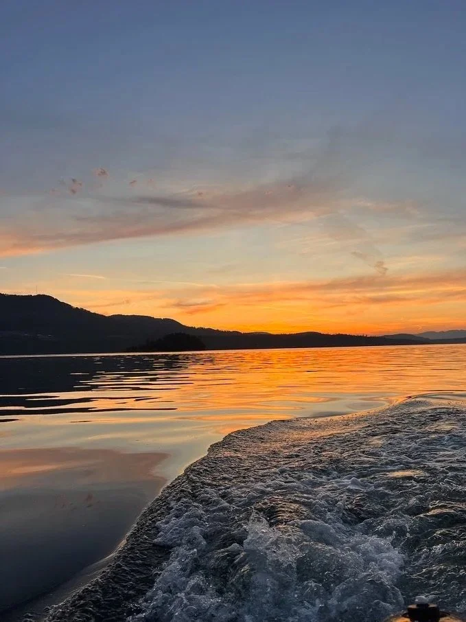Sunset over a lake with mountains in the background, view from a boat with ripples and water spray in the foreground.