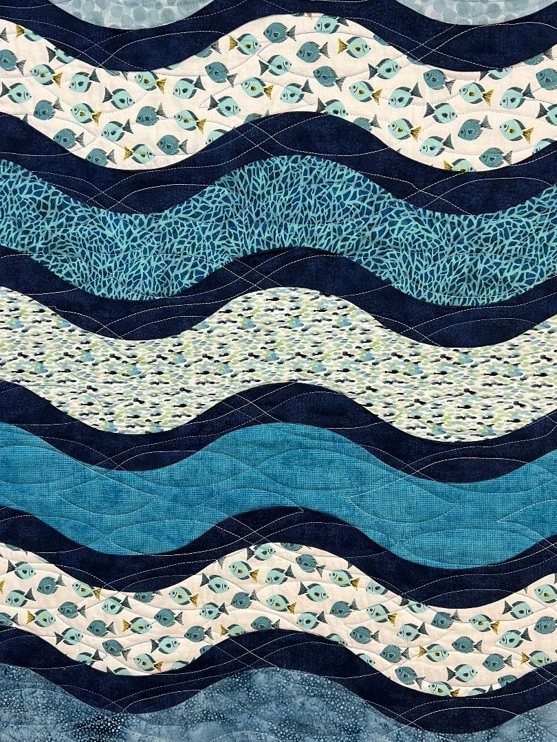 A quilt with wavy patterns in various shades of blue and white, featuring fish and abstract designs.