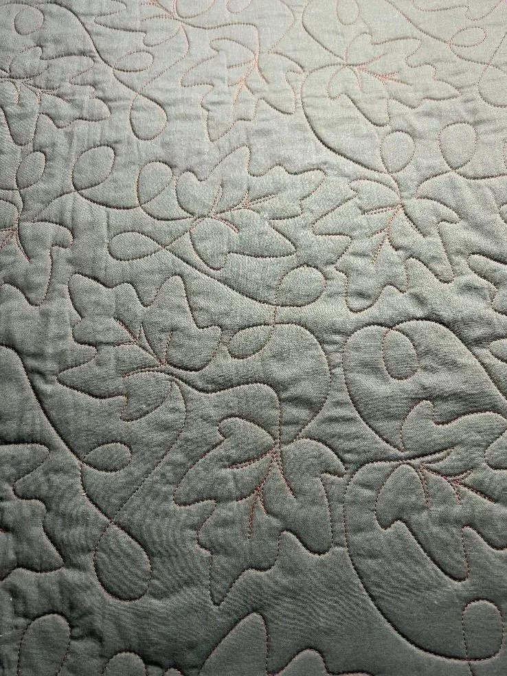 Close-up of a quilted fabric with an oak leaf pattern stitched in pink thread.