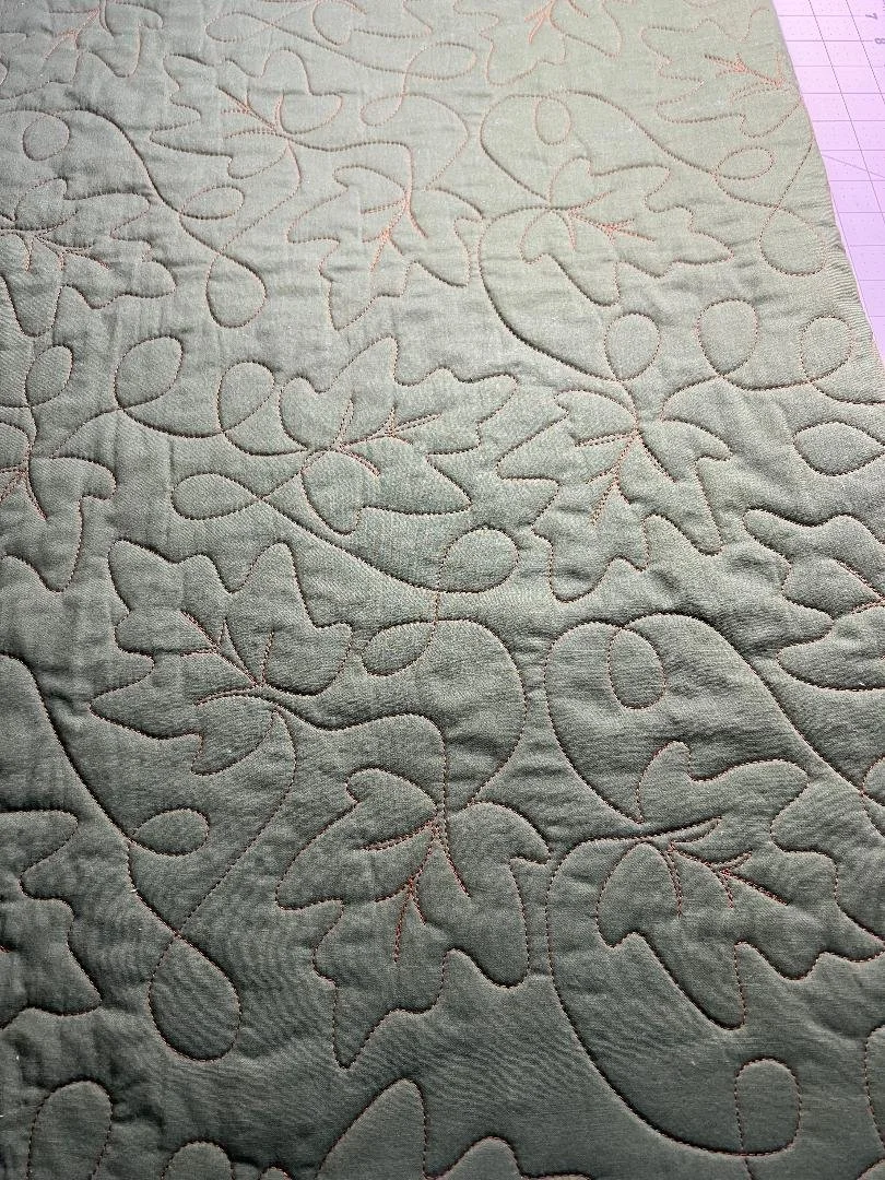 Close-up of quilted fabric with a pattern of leaves and vines.