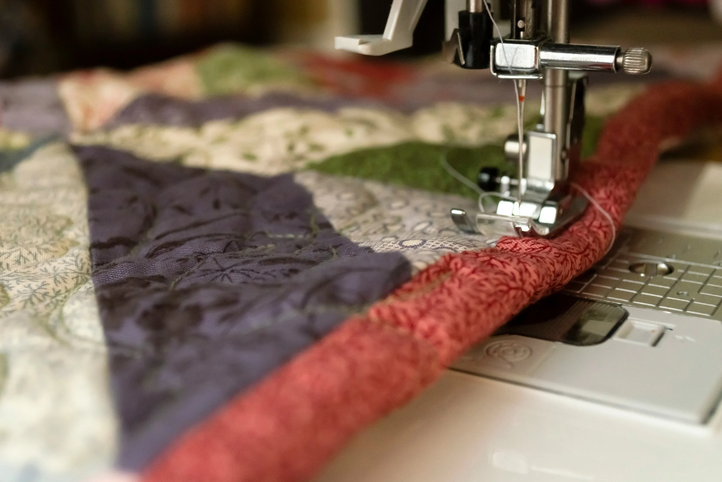 Close-up of a sewing machine stitching together a quilt with multicolored fabric pieces.