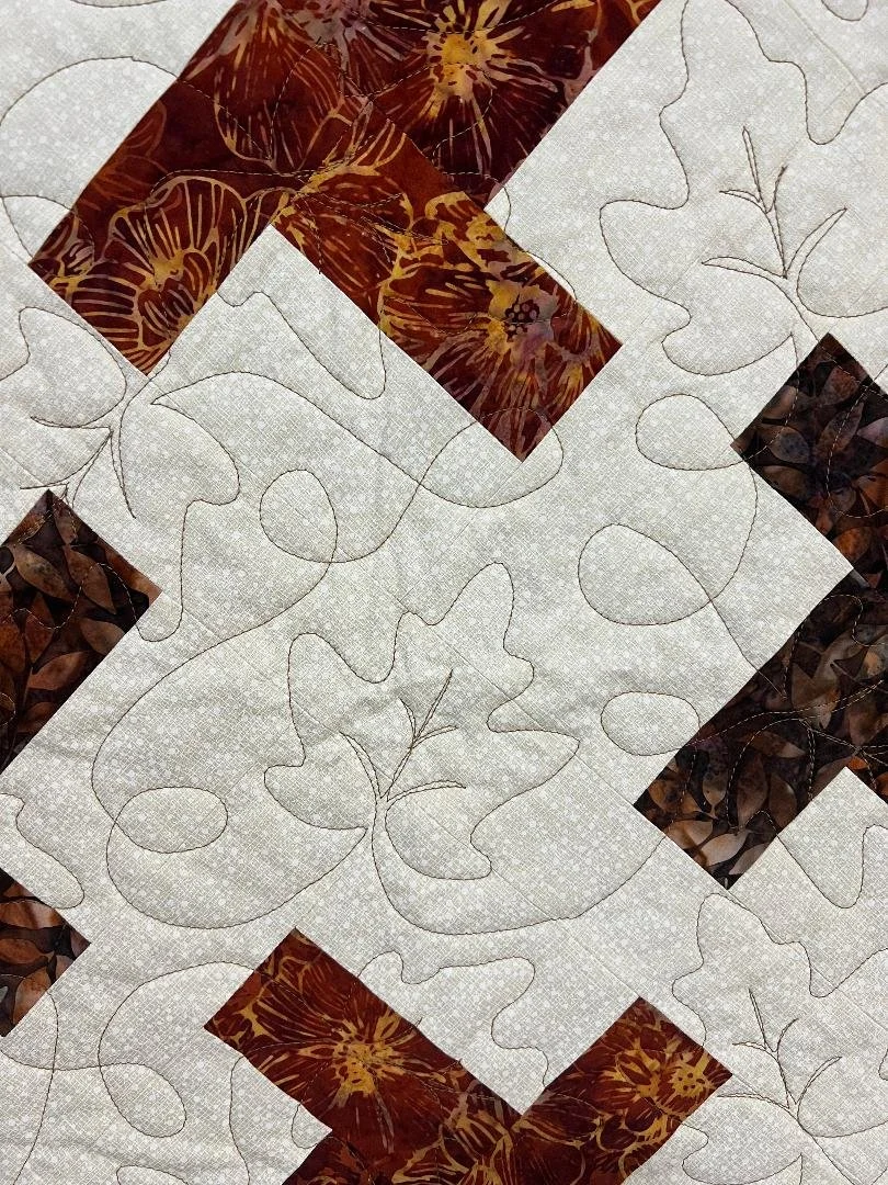 A quilt in progress with hand-stitched outlines of leaves and flowers, featuring fabric pieces with a brown and orange floral pattern sewn onto a light-colored background.