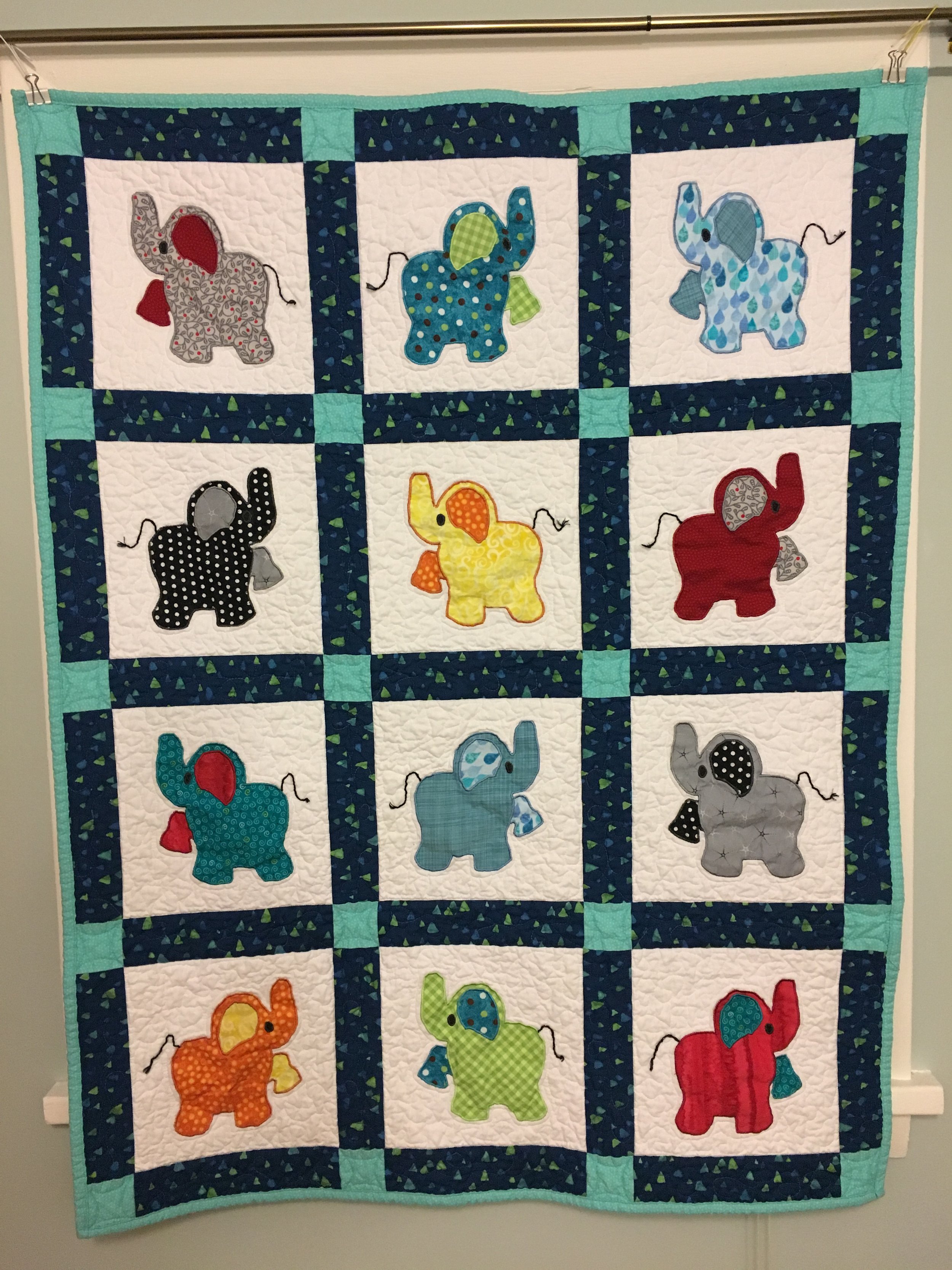 A handmade quilt featuring colorful elephants with different patterns and accessories, bordered with dark blue and light green fabric.
