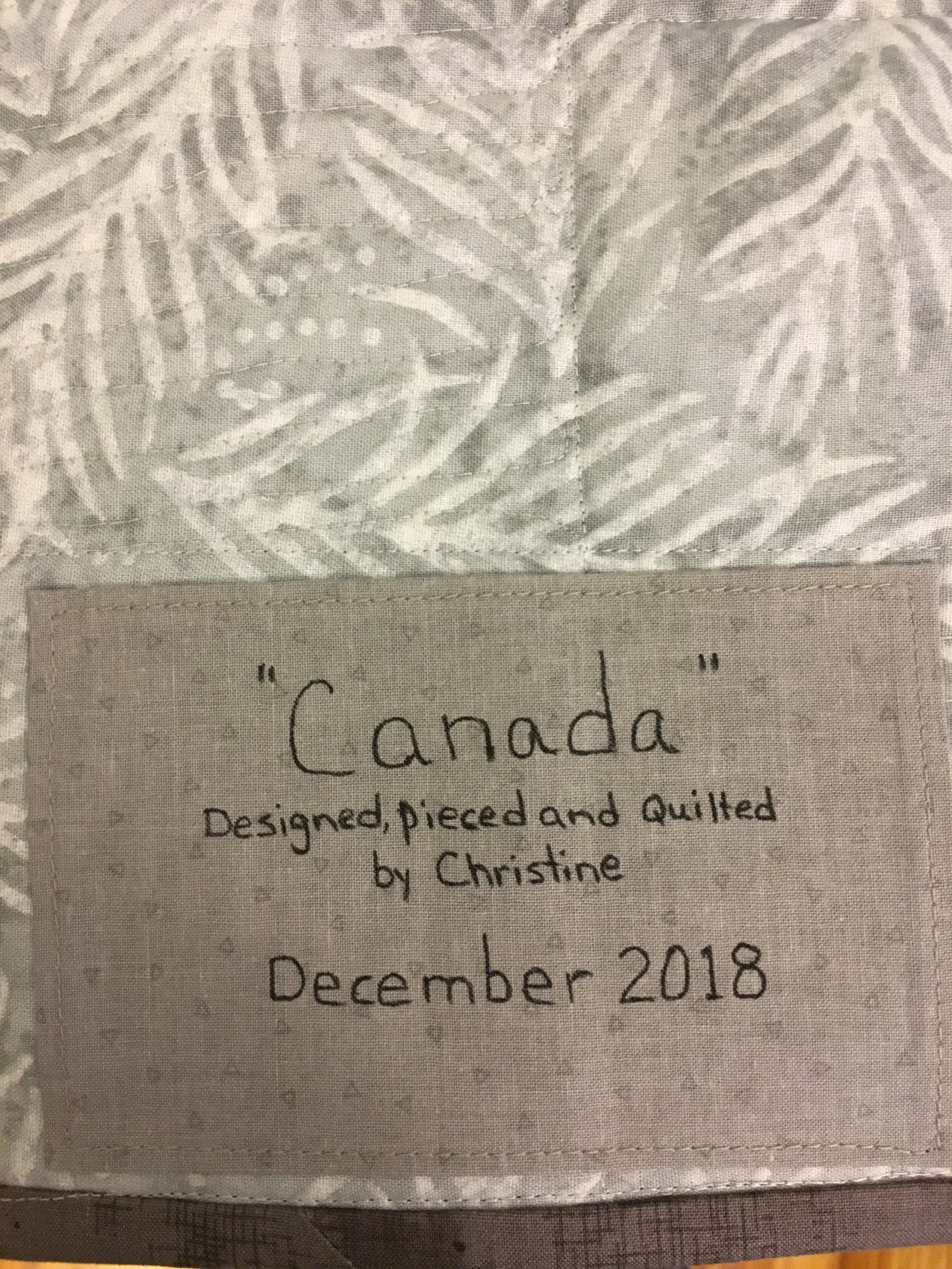Cloth label with text indicating it was designed, pieced, and quilted by Christine in December 2018, titled 'Canada'.