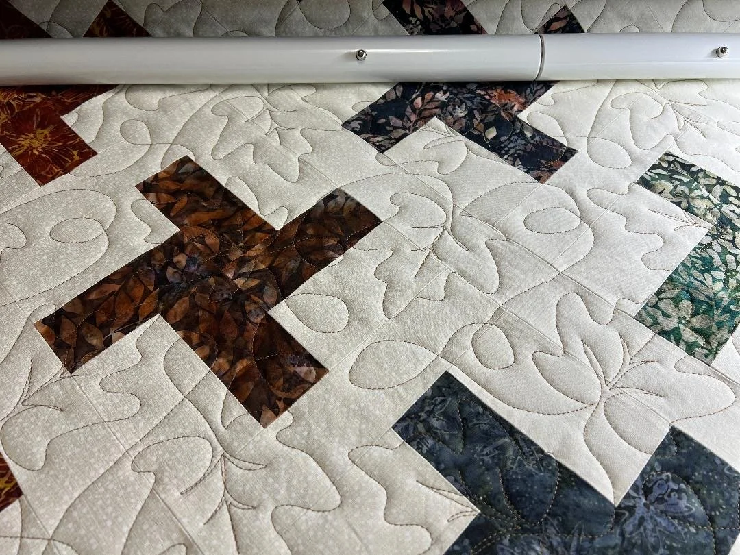 Close-up view of a quilt with leaf and cross patterns in various colors, with a metal rod at the top.