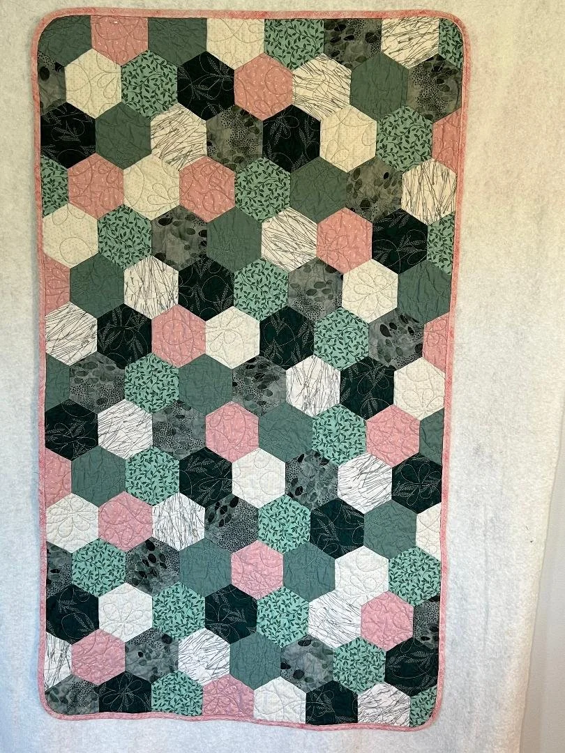 A quilt with a pattern of hexagons in various shades of green, black, white, and pink, with some featuring different leaf and floral designs.