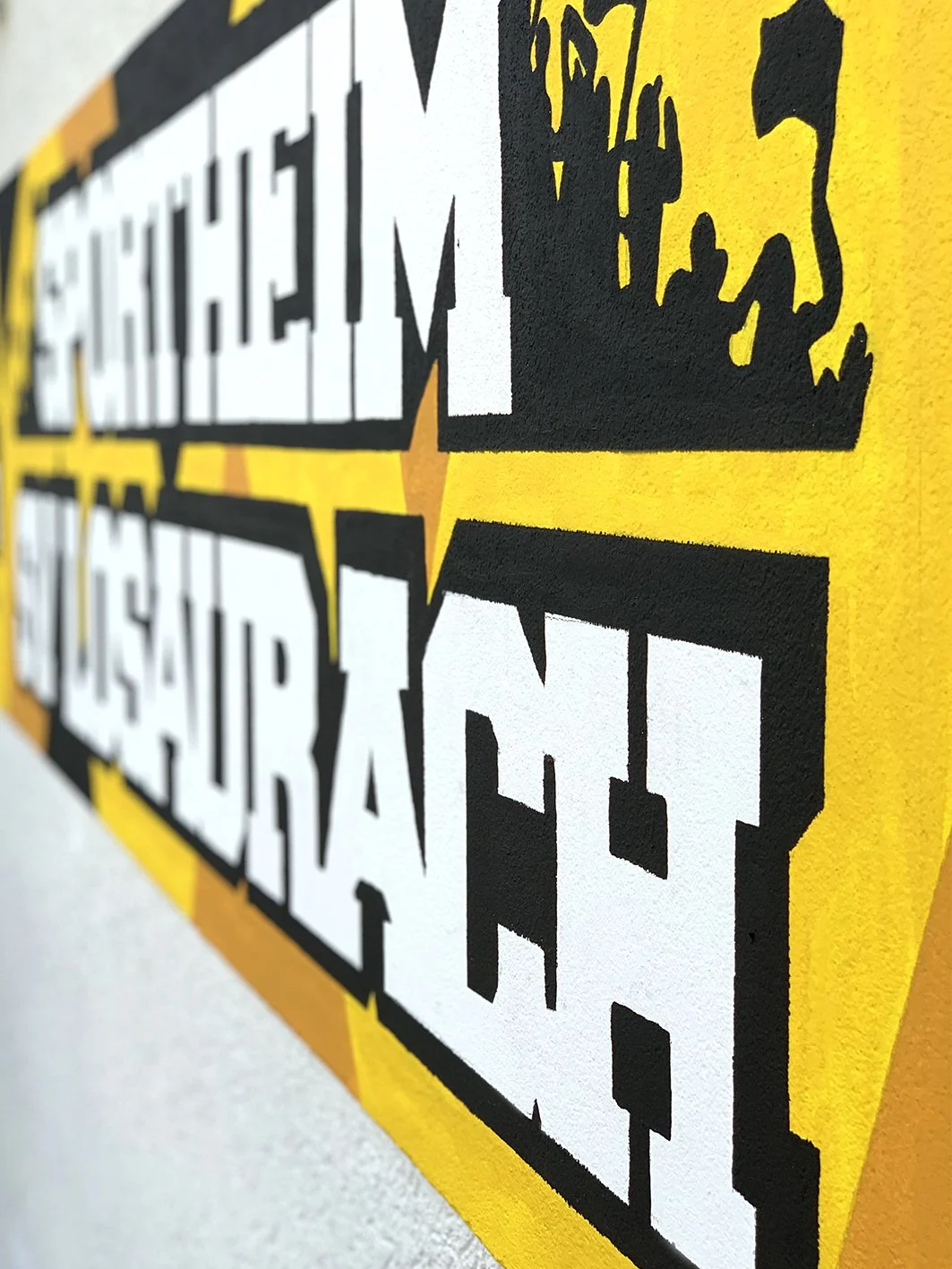 Detail eines großen Graffitis auf der Fassade eines weißen Hauses. Das Graffiti zeigt das Logo und den Namen des Sportvereins SV Losaurach, inklusive gelben Farben und weiteren Wappen in dynamischen Winkel.