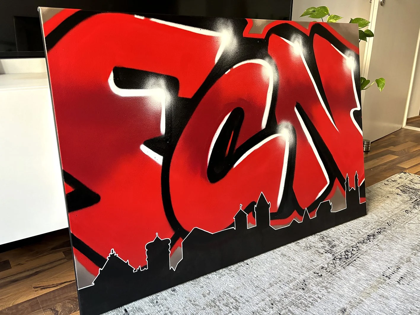 Graffiti-Kunstwerk mit rotem, schwarzem und weißen Farbmustern, darunter eine schwarze Silhouette einer Stadt mit markanten Gebäuden auf einem schwarzen Hintergrund.
