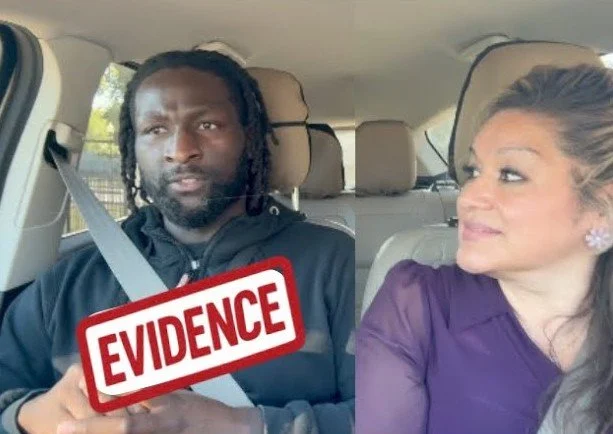 A man and woman sitting in a car. The man is holding a sign that says 'EVIDENCE'. The woman is looking at the man with a slight smile.