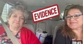 Two women sitting in a car, with a red and white sign reading 'EVIDENCE' above them.