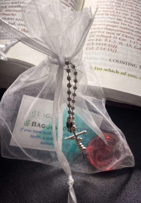 A small gift wrapped in sheer organza fabric, tied with a ribbon, with a metal chain and a small red wax seal attached, placed on top of an open Bible.