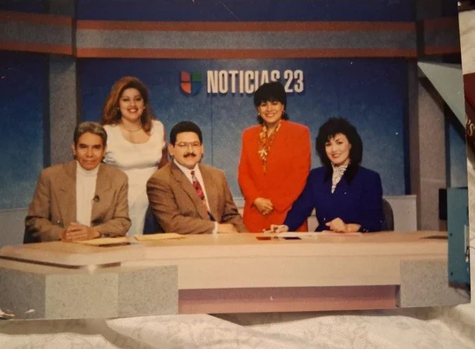 Five news anchors or reporters behind a news desk at Noticias 23 studio.