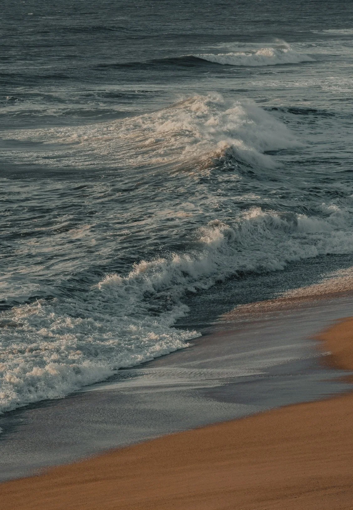 Ocean waves crashing onto a sandy beach at sunset.