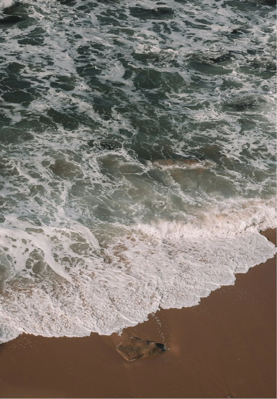 Waves crashing onto a sandy beach with a small rock in the foreground.