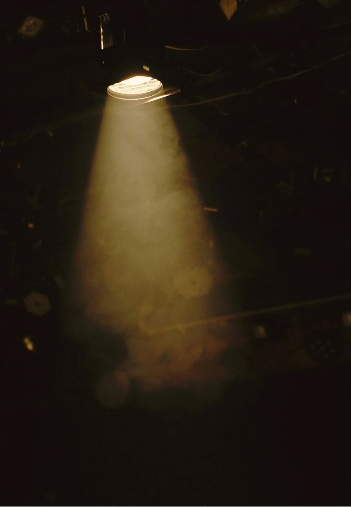 A ceiling vent with a spotlight shining through, revealing dust particles in the air.