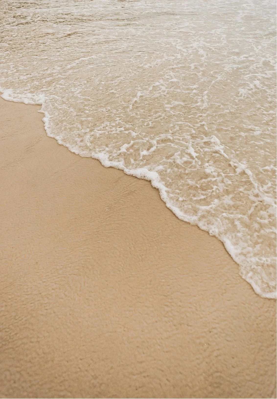 Close-up of a sandy beach with gentle waves washing ashore.