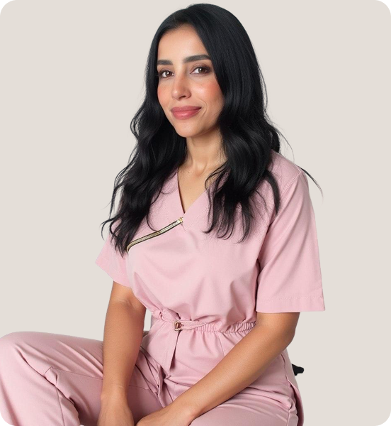 A woman with long black hair, wearing a pink medical uniform, sitting against a plain light background.