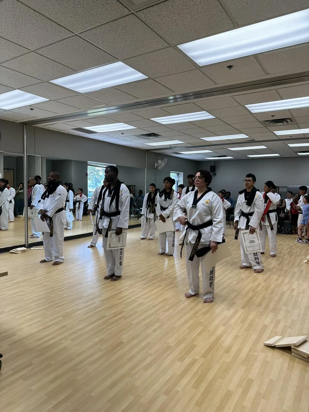 Adult and teen students standing in formation holding their belt promotion certificates during a belt testing ceremony at Will Brown's Taekwondo.