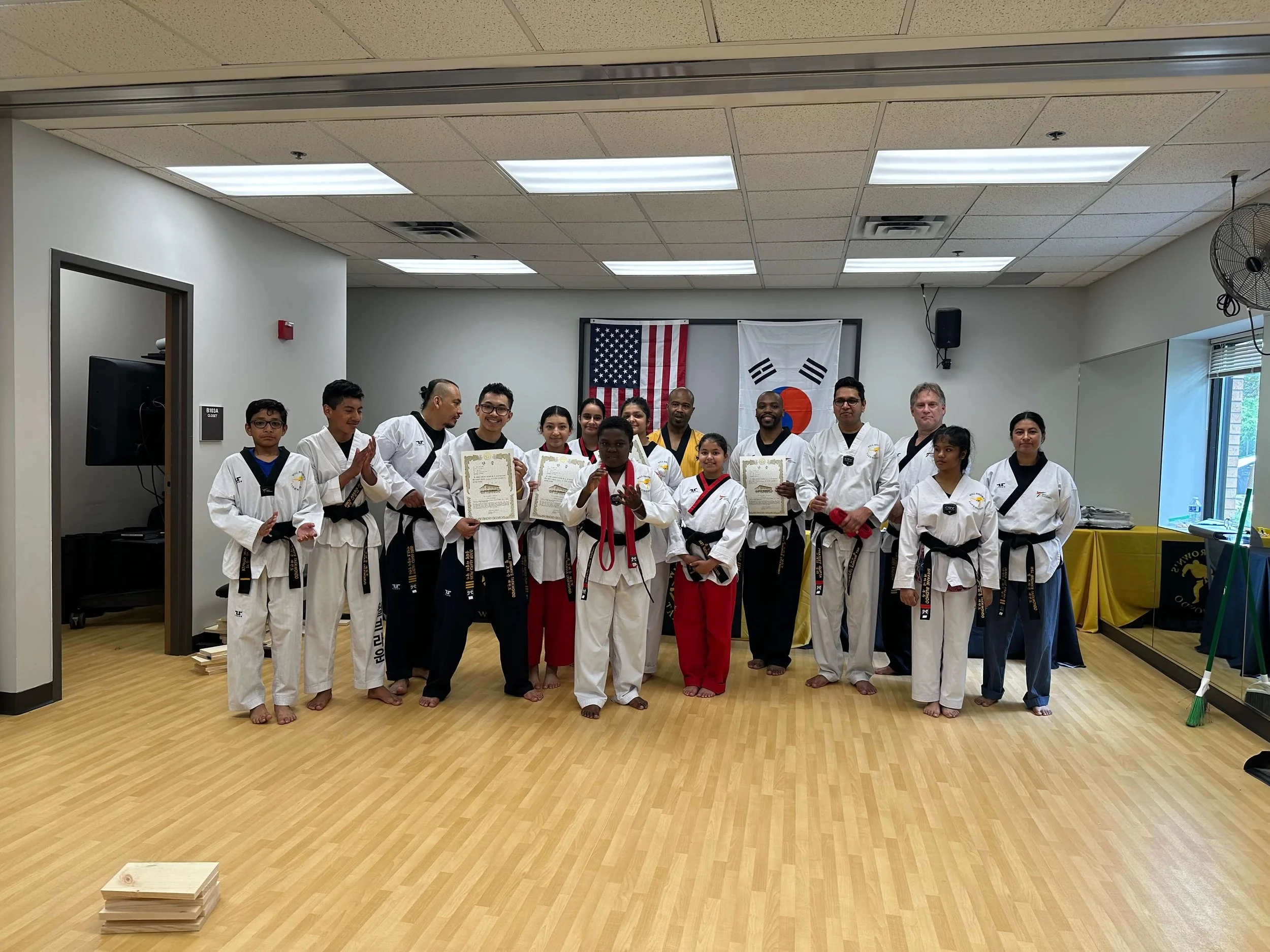 Master Will Brown and a group of students and instructors at Will Brown's Taekwondo pose together after a belt testing ceremony. Several students are holding certificates.