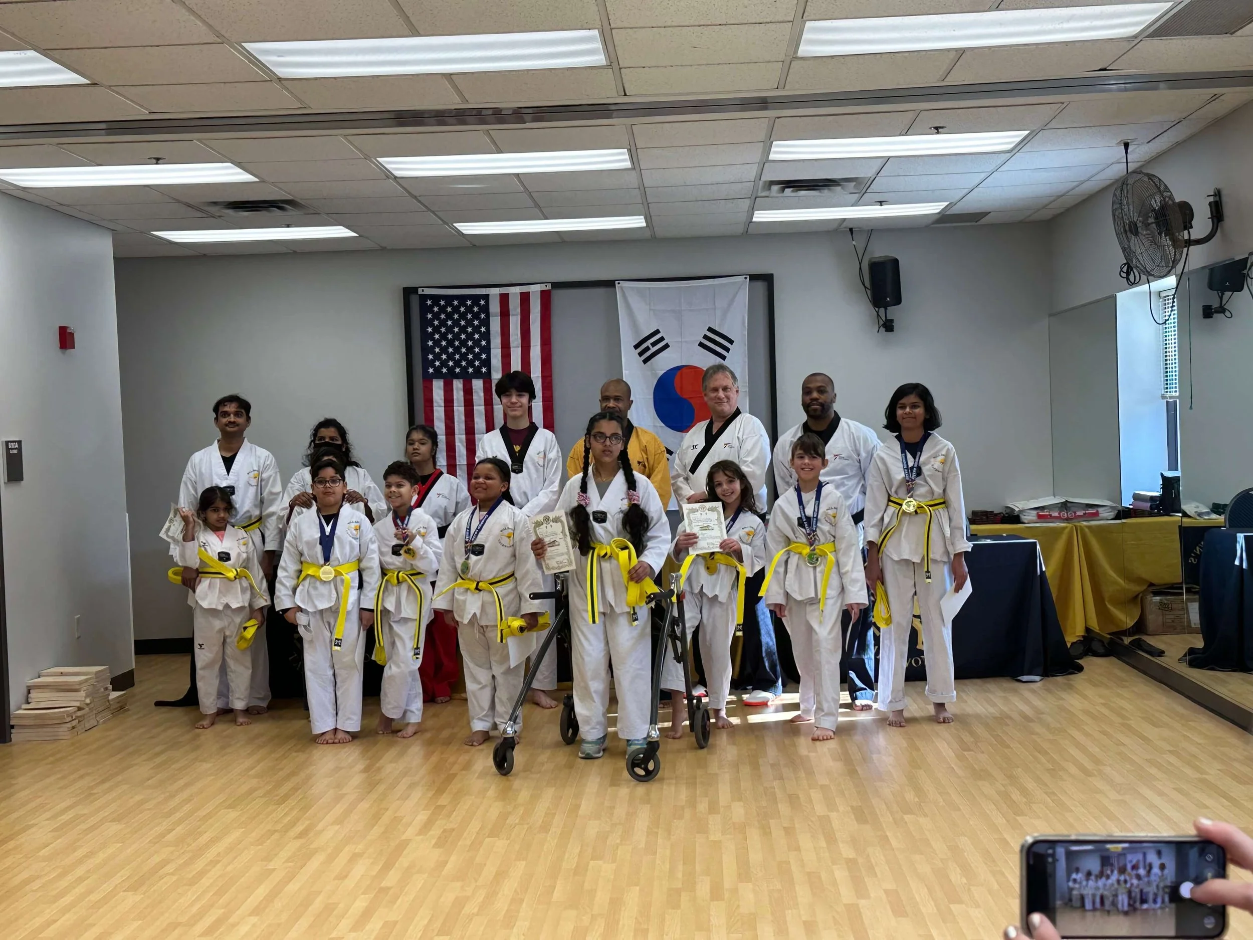 Students, instructors, and Master Will Brown pose together after a belt testing at Will Brown's Taekwondo. Several students are holding medals and certificates.