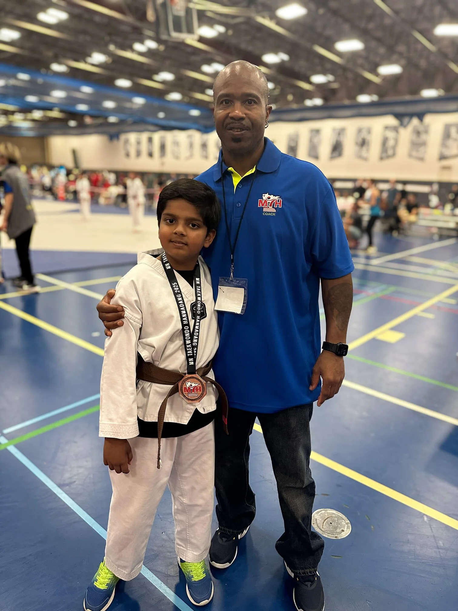 Master Will Brown posing with a young student wearing a brown belt and a tournament medal at the Minnesota Taekwondo Hanmadang.
