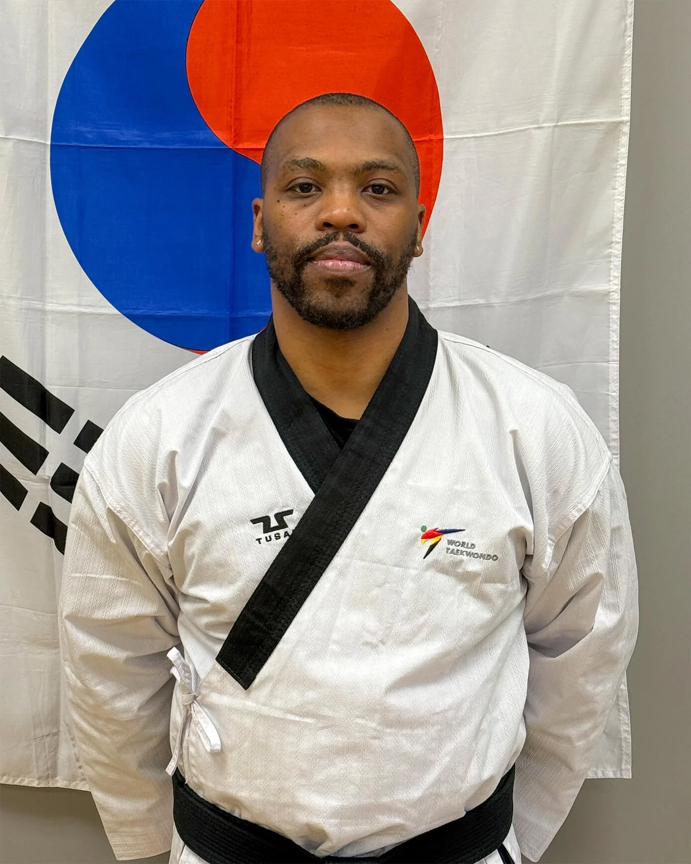 Anthony Brown, an African American man, is  wearing a Taekwondo uniform and standing in front of a Korean flag.