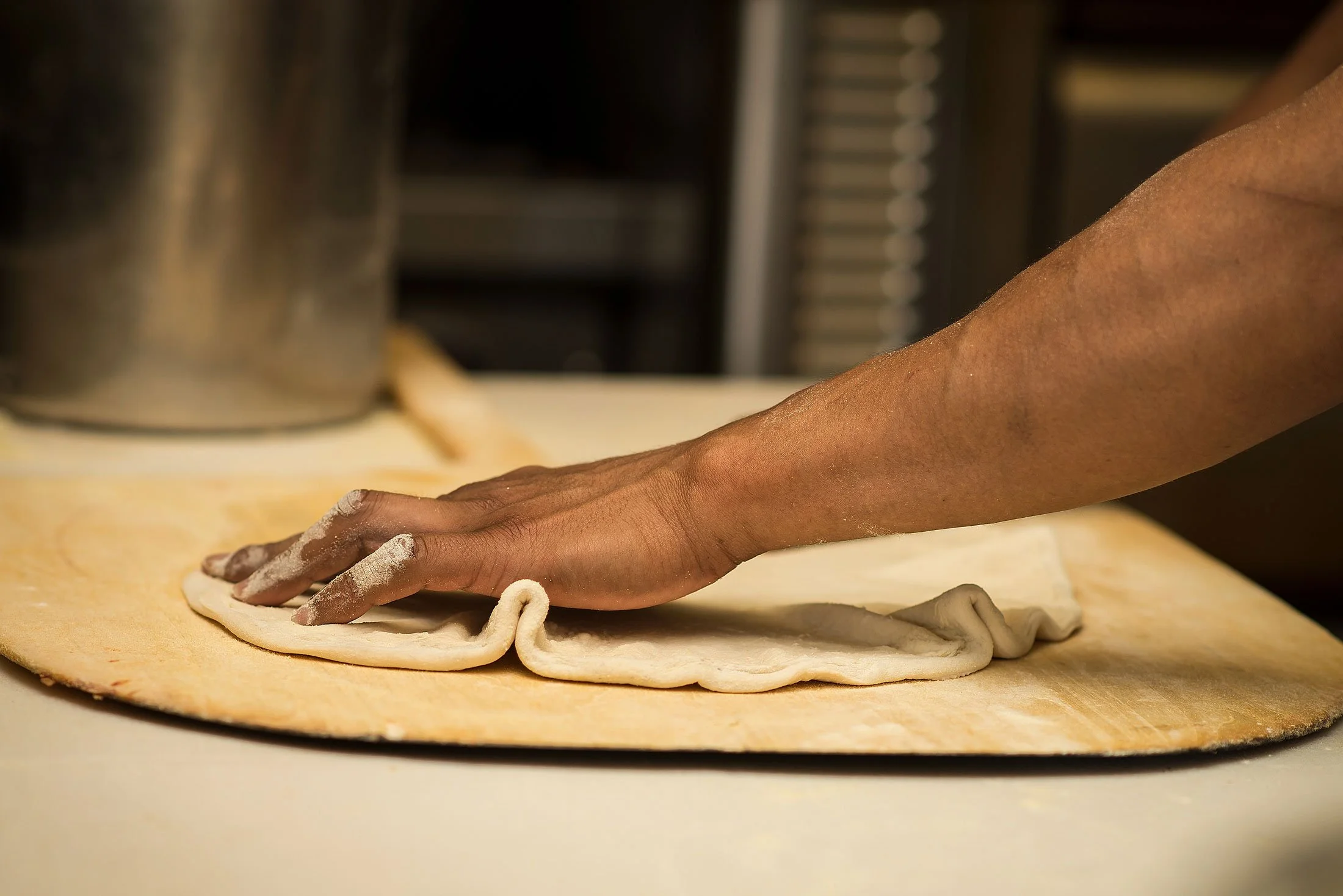 A person is kneading dough on a floured wooden surface in a kitchen.