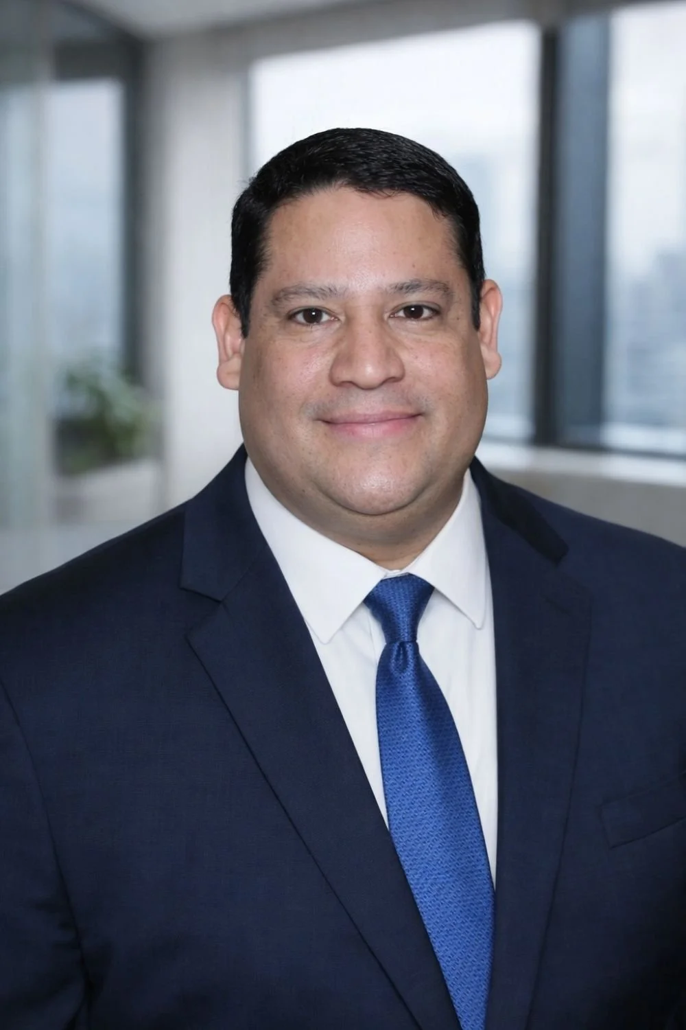 A man in a suit and tie smiling at the camera in an office setting.