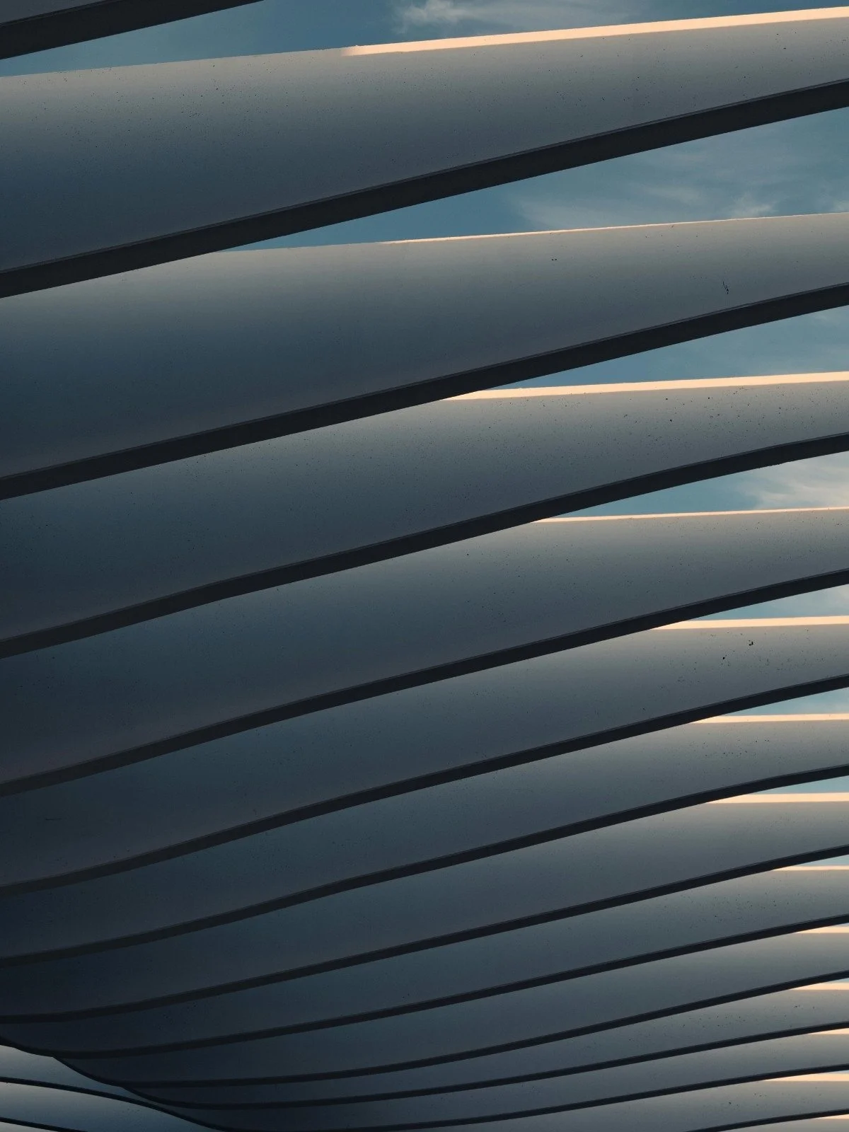 Close-up view of exterior metallic sunshade panels with sky reflection, aligned in parallel lines.