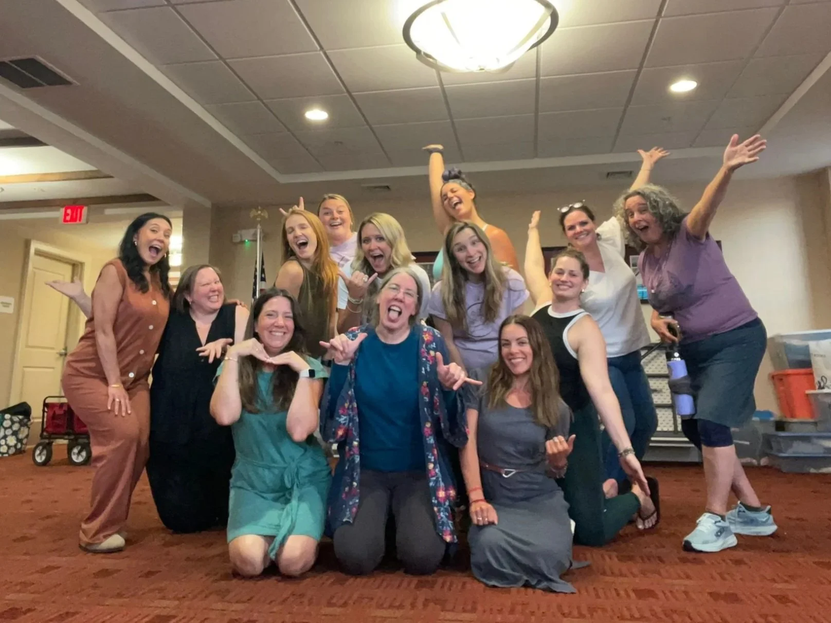 Group of smiling women posing together indoors, some standing and some kneeling or sitting, celebrating and having fun.