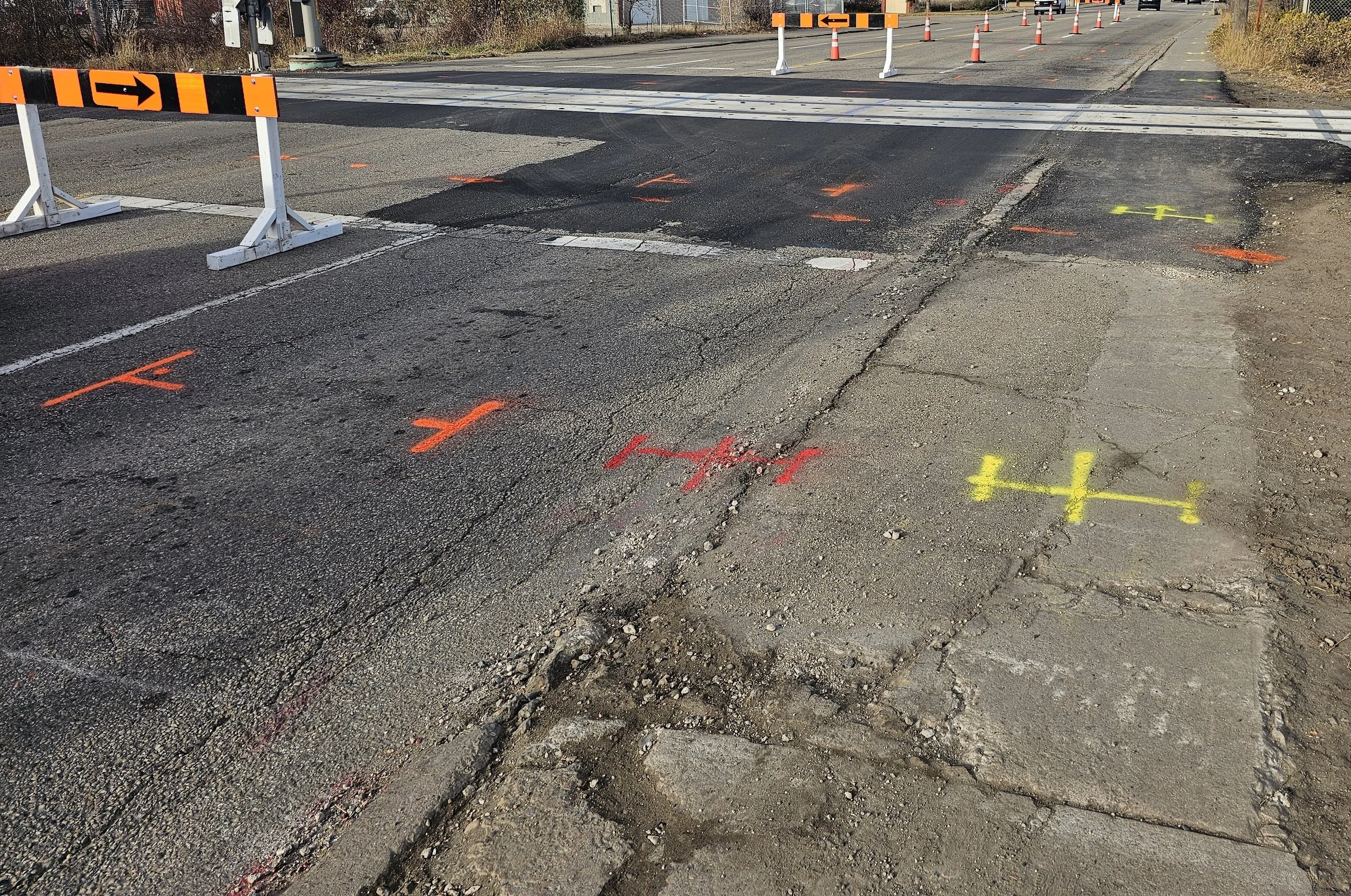 Construction zone on a road with traffic barriers, orange markers, and pavement markings in orange and yellow identifying underground utilities