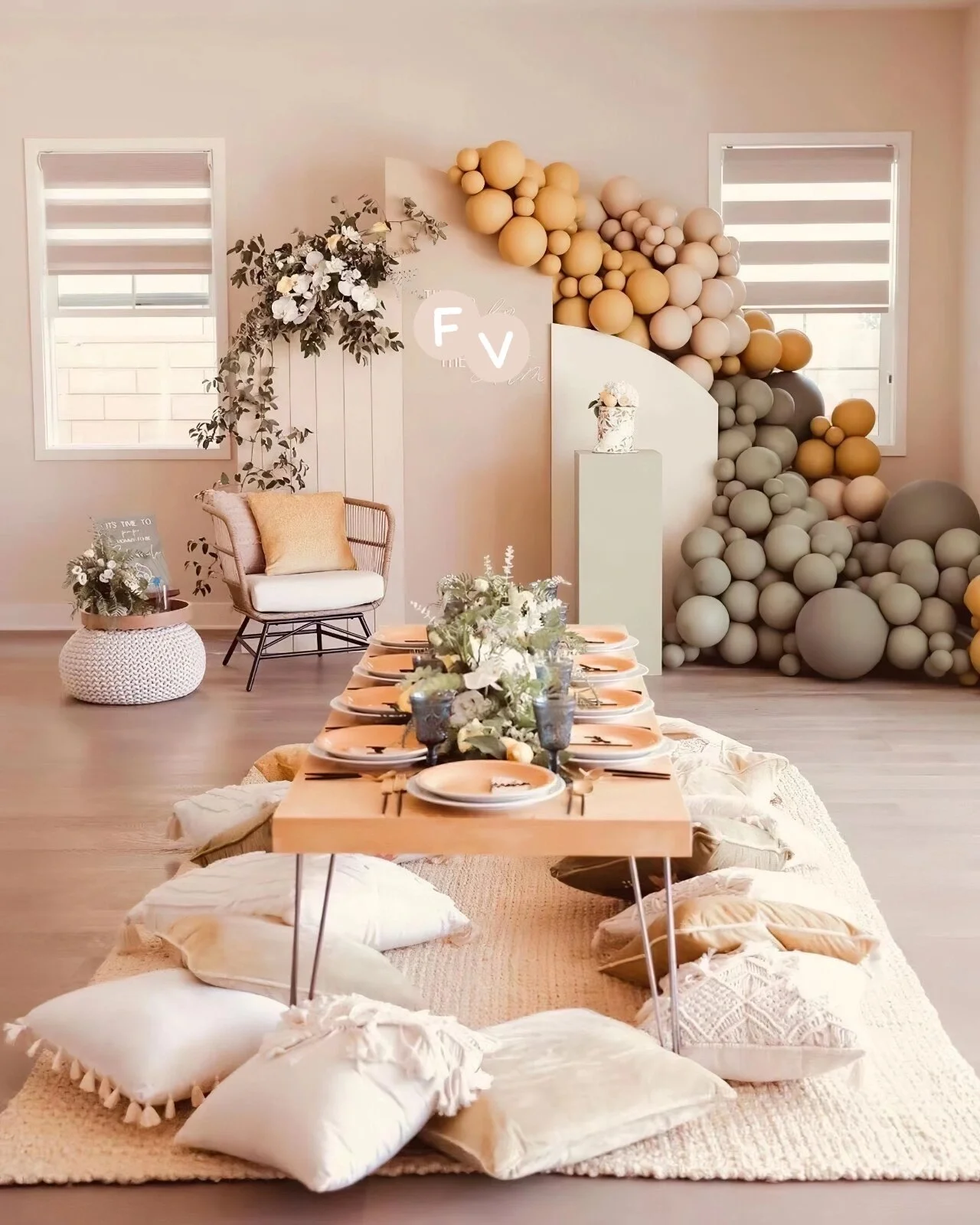 Decorative room with table set on floor with pillows underneath, surrounded by a seasonal display of balloons, flowers, and seating area.