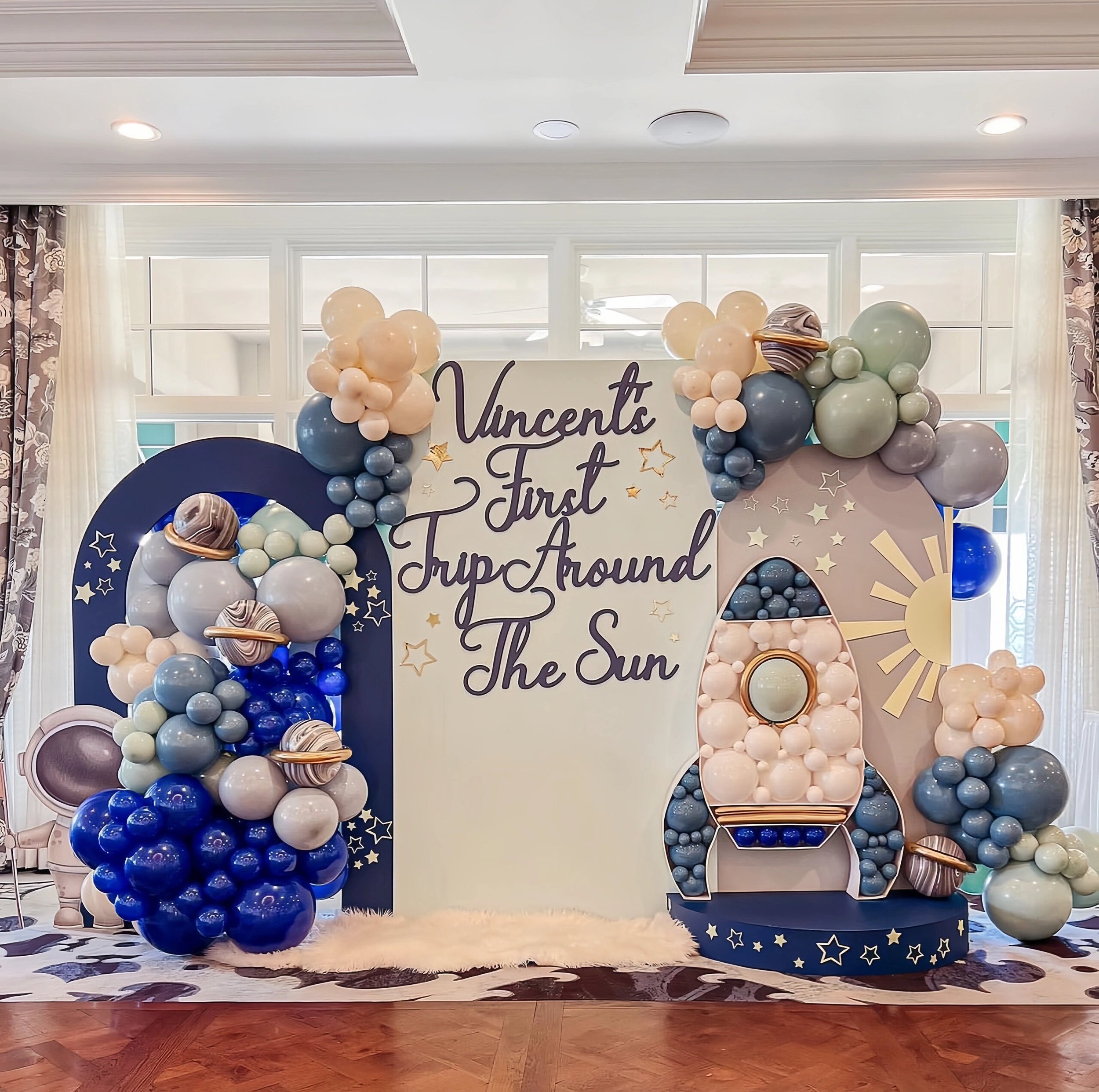 Decorative backdrop with balloons, planets, and stars celebrating a child's first trip around the sun.