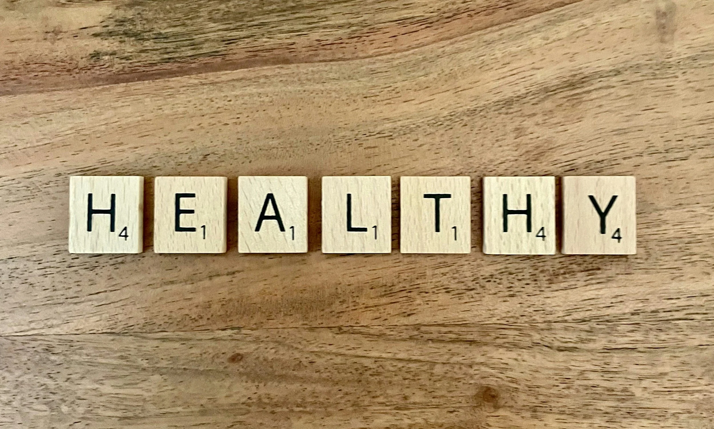 Scrabble tiles spelling out 'HEALTHY' on a wooden surface.