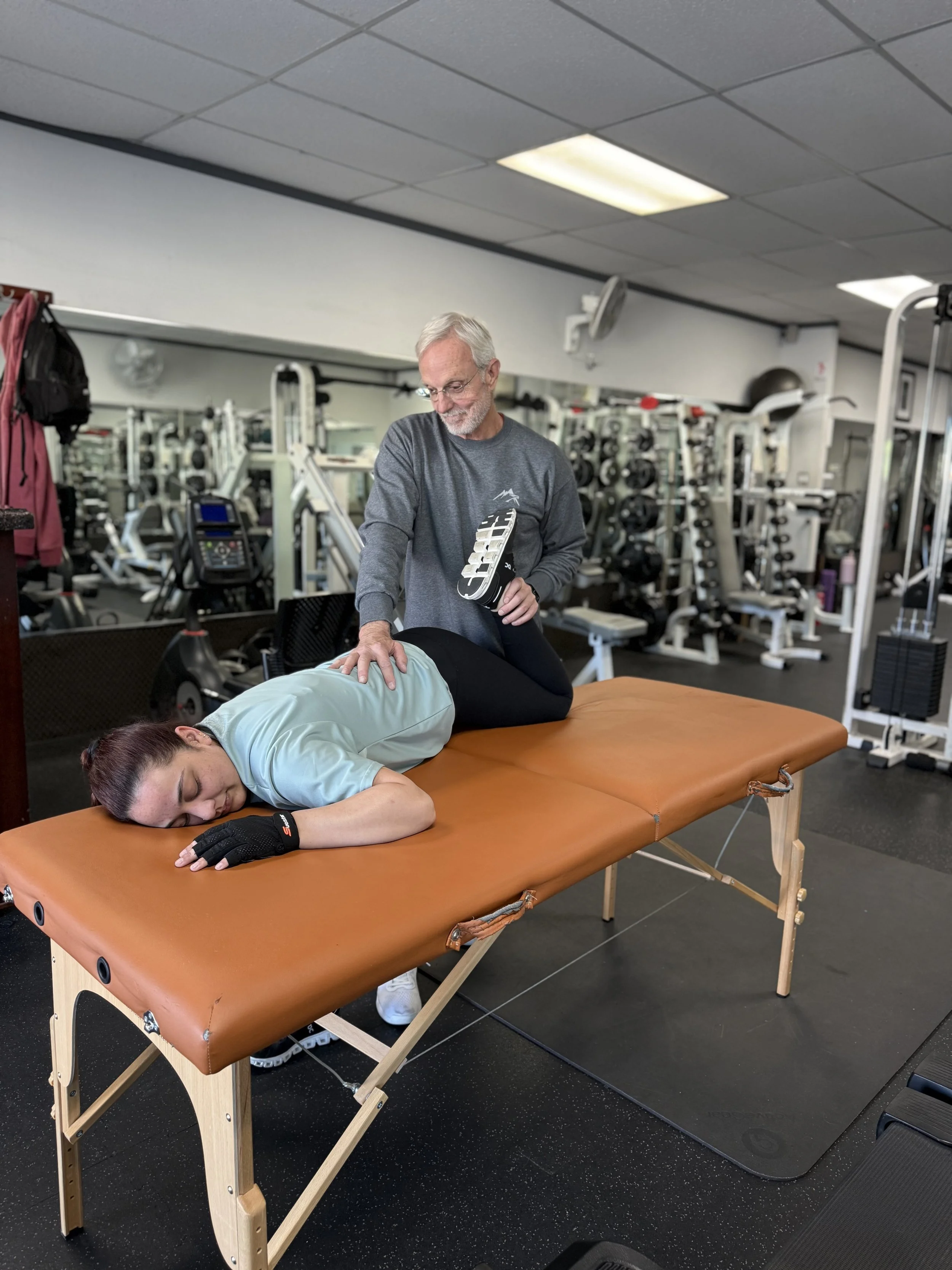 A person receiving a massage or physical therapy from a therapist on a massage table in a gym or fitness center.