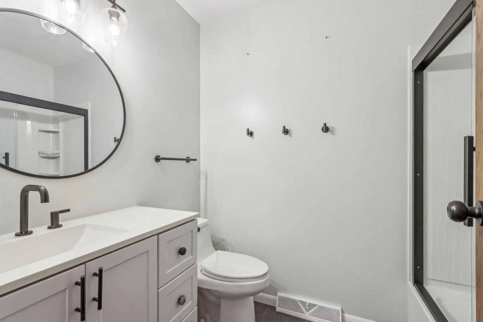 Bathroom with white vanity, oval mirror, wall-mounted light fixtures, and a walk-in shower with a glass door.