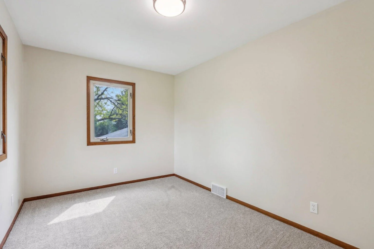 Empty room with beige walls, carpeted floor, and two windows with wooden trim letting in natural light.