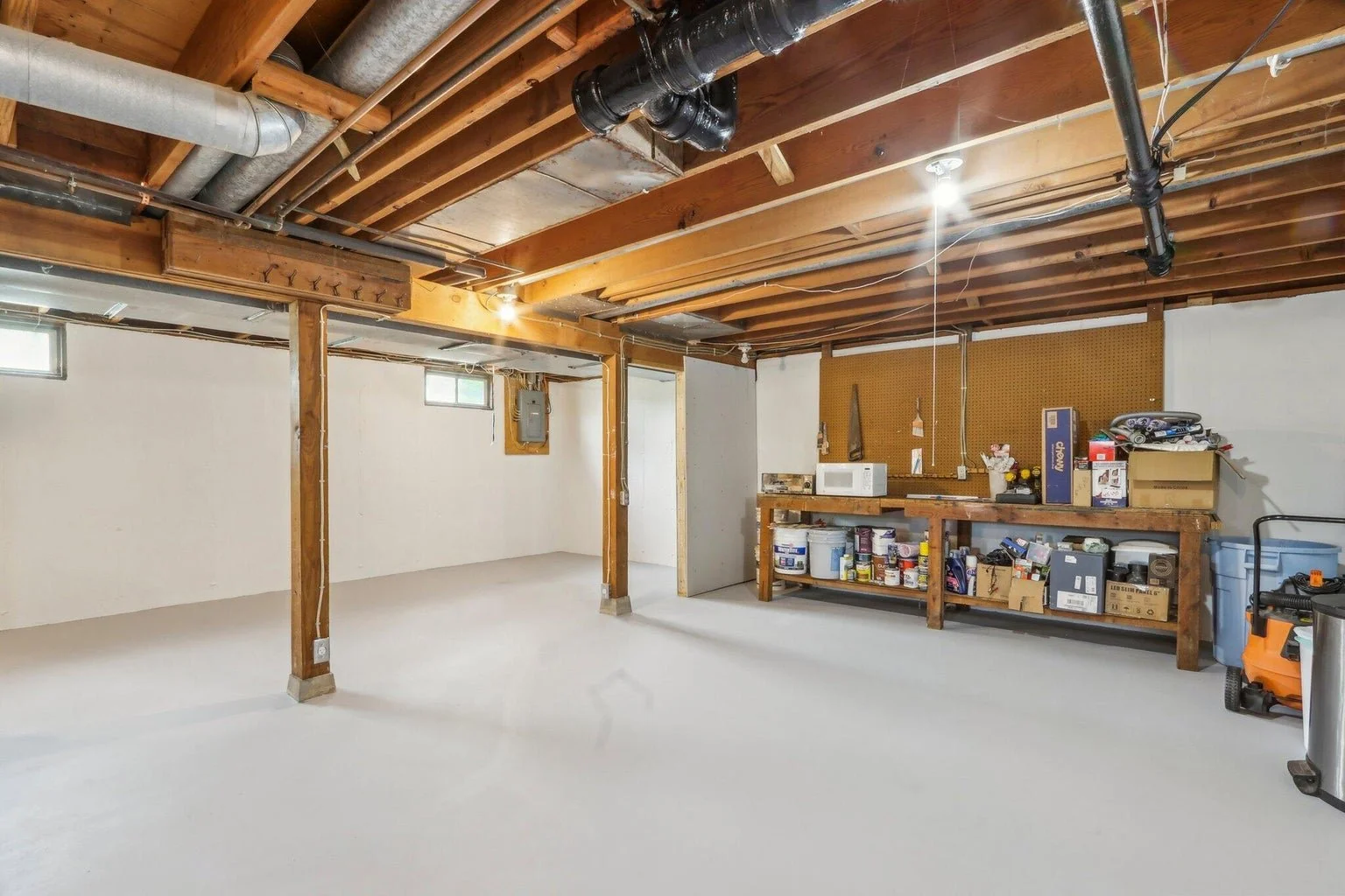 Empty garage with wooden ceiling, white walls, small windows, and a workbench with tools and storage bins.