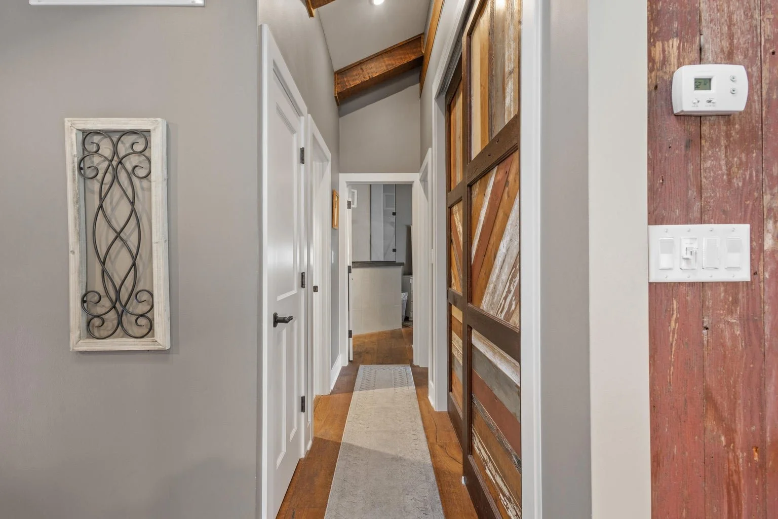 Hallway with light gray walls, white doors, a beige runner rug, and a rustic sliding barn door made of reclaimed wood.