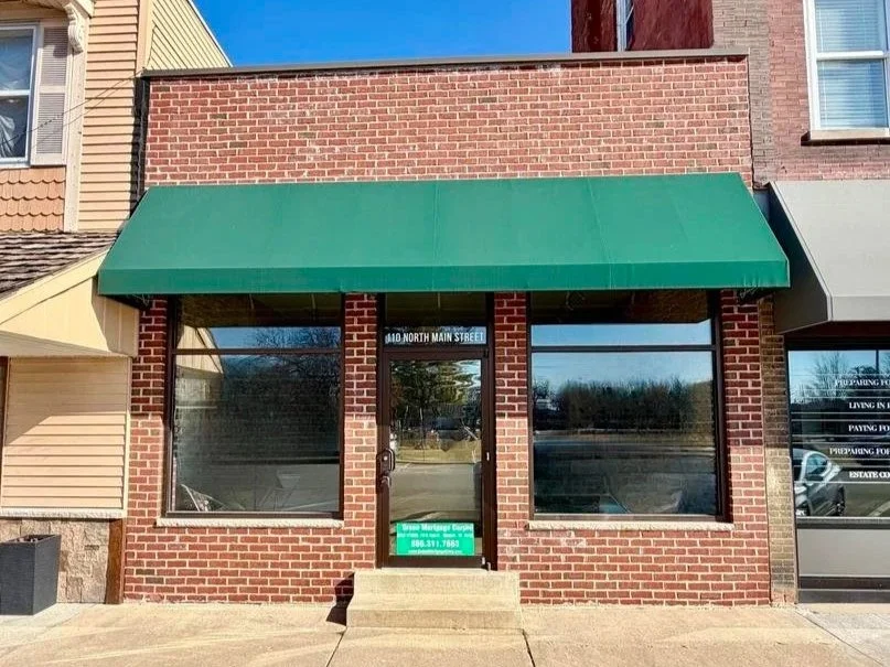 Facade of a small commercial building with a green awning, glass door, and large windows located at 410 North Main Street.