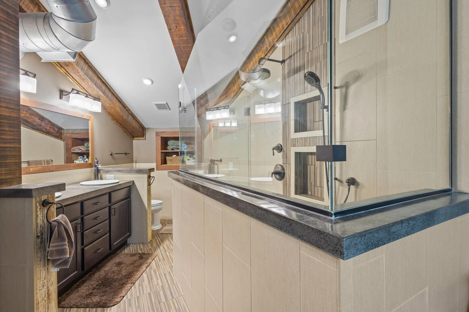 A modern bathroom with a glass-enclosed shower, a dark wood vanity with a single sink, a large mirror, beige tiled walls and floor, and wooden accents on the ceiling and shelves.