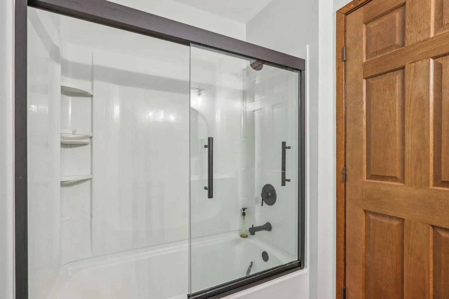 Bathroom shower with glass doors, black fixtures, and a wooden door to the right.