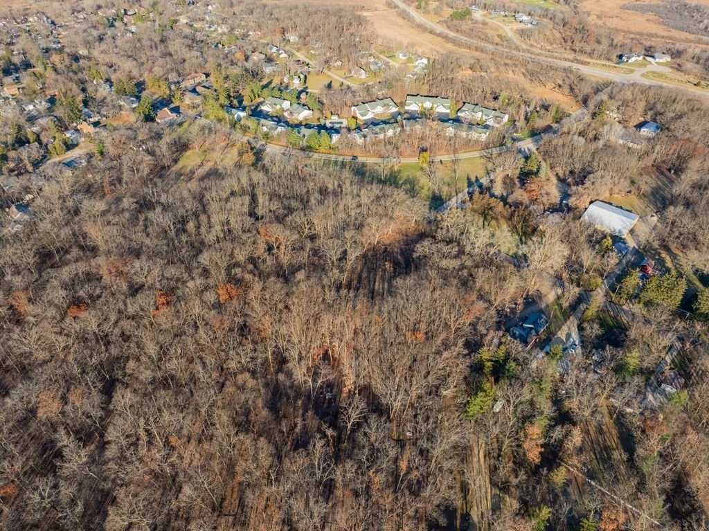 Aerial view of a wooded area and residential neighborhood with houses, trees, and roads in a suburban setting.