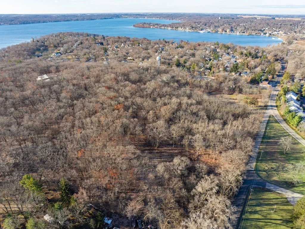 Aerial view of a wooded area next to a lake with houses and roads surrounding it.