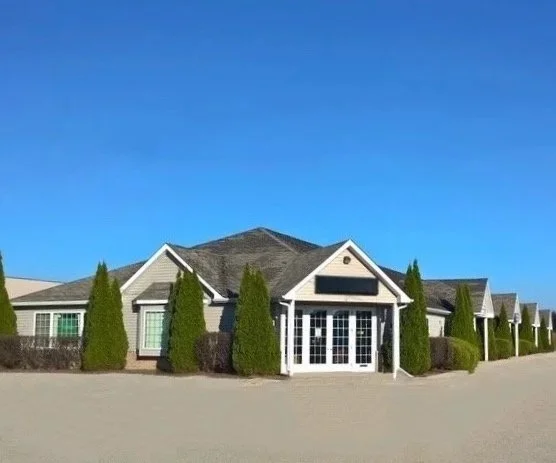 Single-story building with a gable roof, surrounded by tall, trimmed bushes, under a clear blue sky.