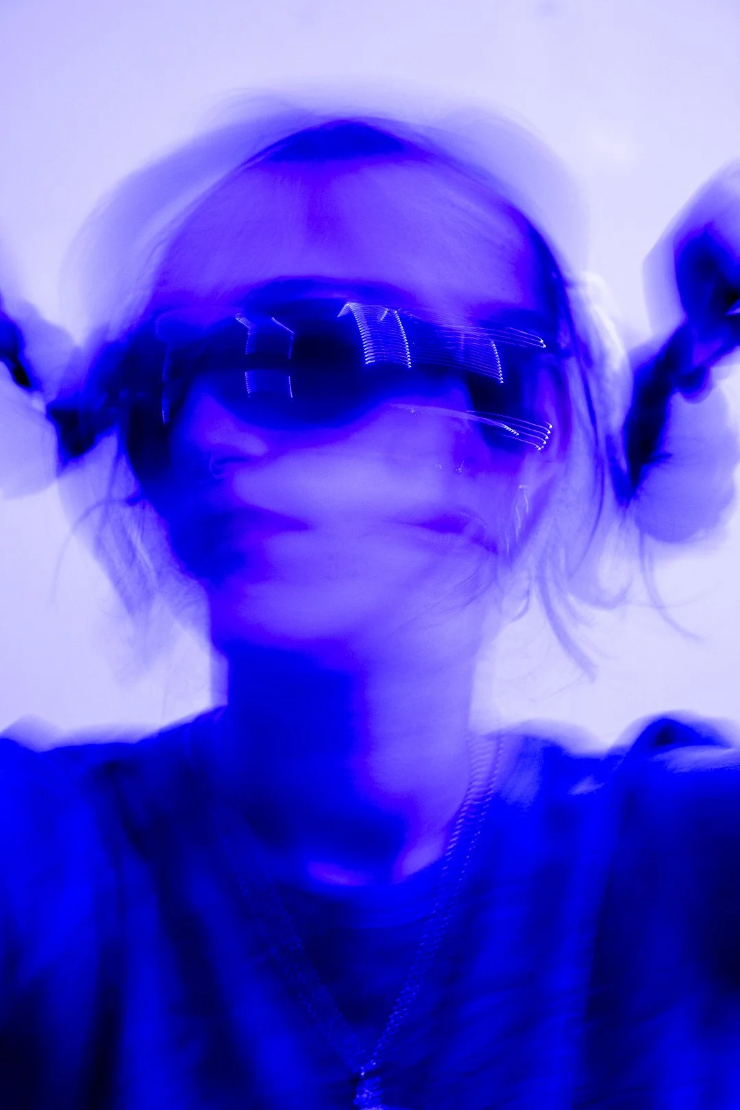 Person with sunglasses, captured with a motion blur effect, illuminated in blue lighting.