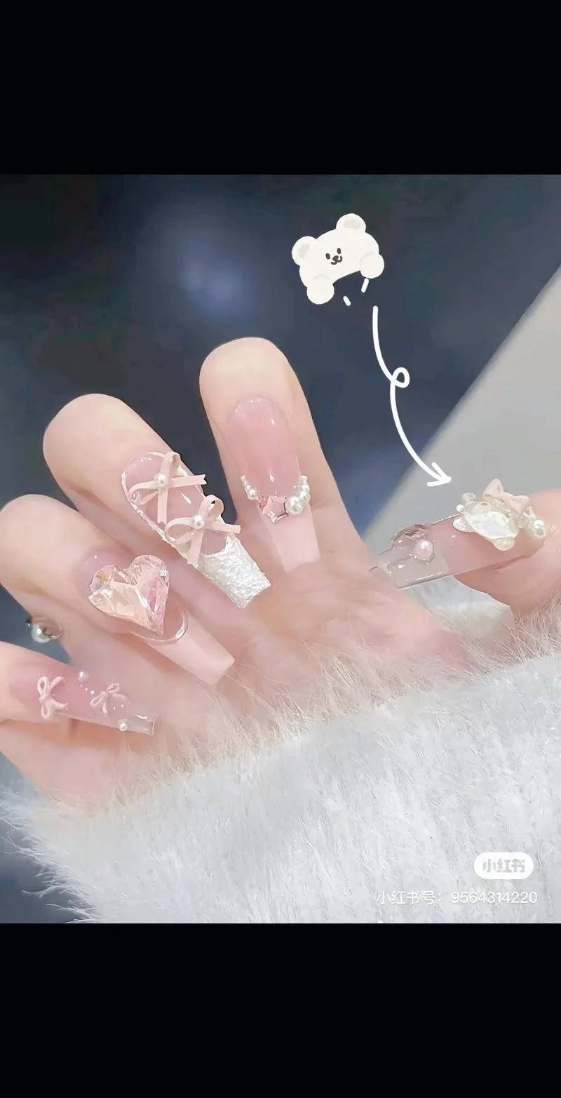 Close-up of a hand with decorated nails featuring bows, pearls, hearts, and lace designs, with a cartoon teddy bear drawing pointing to the nails.